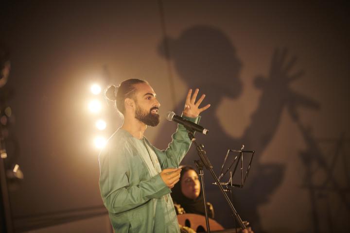 photographie de Rohan Houssein, debout devant un micro, en plein slam poésie